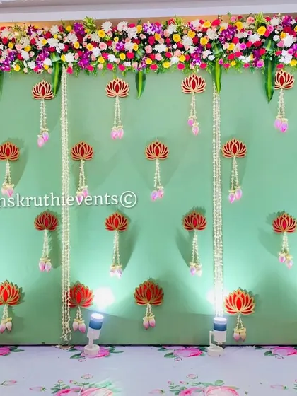 A simple yet elegant naming ceremony backdrop with a pastel green background and hanging lotus motifs. The floral printed floor and side bouquets complete this charming setup.