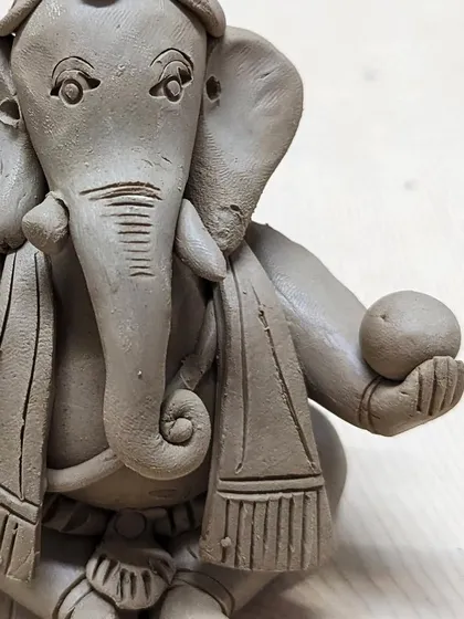A close-up of a detailed clay Ganesha, complete with a shawl and a laddoo, made in our festive workshop.