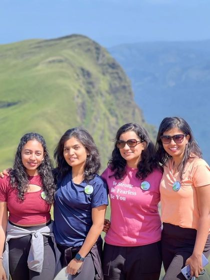 A group of friends smiling for a photo against the clear blue sky and green hills of Netravathi.