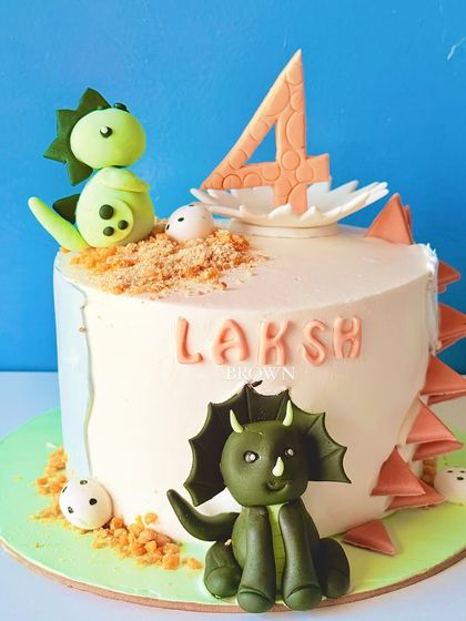 A cute dinosaur-themed cake for a 4th birthday. This design features friendly fondant dinosaurs, a nest with eggs, and edible "dirt" for a fun, prehistoric look.