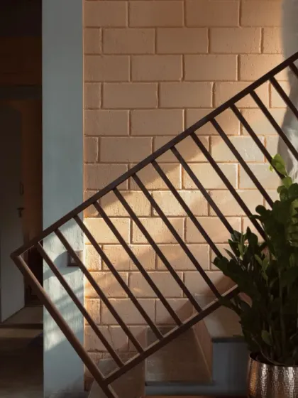 The interplay of light and shadow on an exposed brick wall next to a staircase reveals the raw, honest beauty of the materials used in this vernacular home.