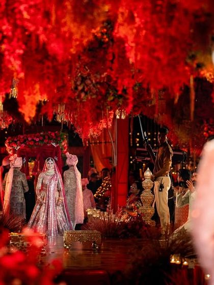 A view from the groom's perspective as his bride makes her way down the aisle. The sea of red florals and warm lighting created an intensely romantic and dramatic atmosphere, a perfect setting for the beginning of their forever.