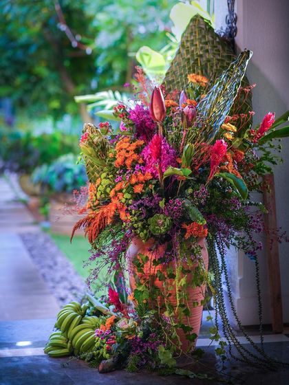 A large, colorful floral arrangement in a terracotta pot, welcoming guests to a Pellikuthuru ceremony.