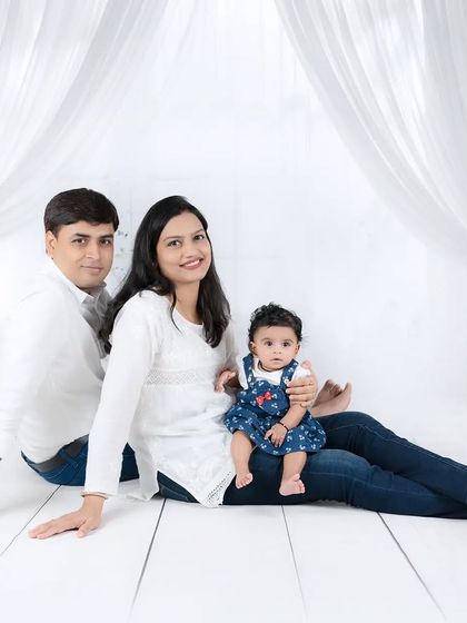 A sweet family of three seated on the floor. The baby girl in her denim dress is the adorable center of this loving family portrait.