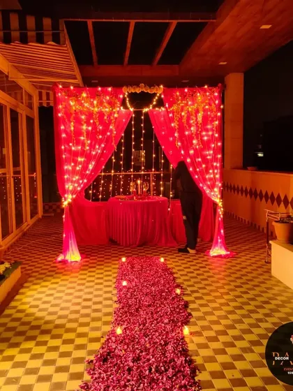 A terrace transformed for a Valentine's dinner, with a red curtained backdrop, fairy lights, and a long pathway made of red rose petals.