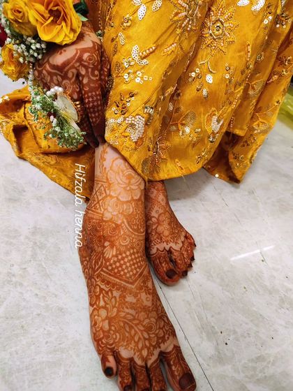 A close-up of the bride's feet, showing how the intricate design complements her stunning yellow mehendi ceremony outfit.