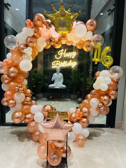 A beautiful rose gold and white balloon ring for a sweet 16th birthday. The setup includes a crown foil balloon, a neon sign, and a number '16' balloon.