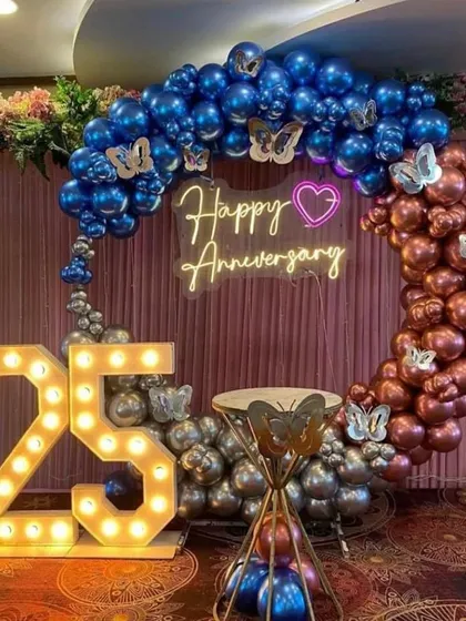 A 25th-anniversary setup with a balloon ring in metallic blue, bronze, and silver, decorated with butterflies and a neon sign.