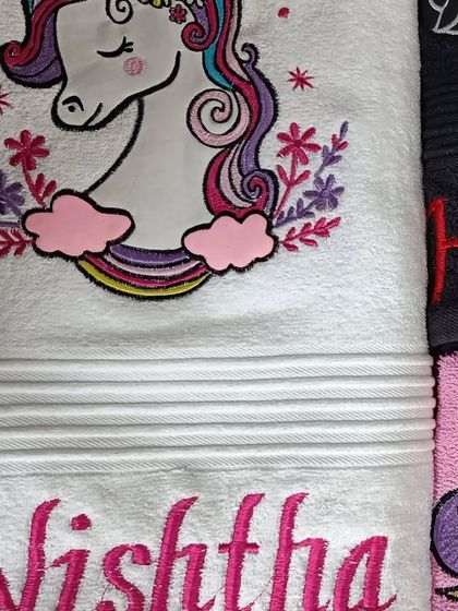 A beautiful white towel with a unicorn embroidery and the name 'Nishtha' in pink.