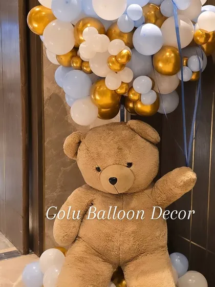 A life-sized teddy bear holding a large bunch of balloons, a perfect prop for photos at a first birthday party.