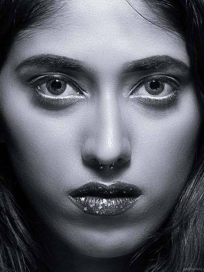 An intense black and white close-up portrait. The direct gaze and glitter on the lips create a captivating and memorable beauty shot.