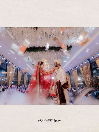A spectacular wide shot of the Varmala ceremony, with the couple on a raised platform amidst a shower of confetti and smoke.