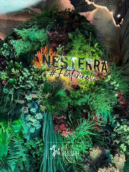 The illuminated Nesterra brand name and hashtag glowing from within a massive wall of dense, varied greenery. This living wall served as the central branding element for their showroom event.