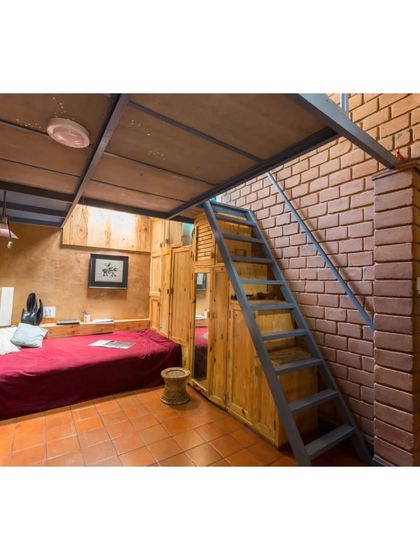A cozy bedroom in the Sans Souci Residence featuring a mezzanine level to maximize space. The tall volume enhances cross-ventilation, and the use of natural materials like wood and earth creates a warm, healthy living environment.
