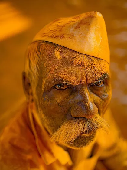 A striking portrait of a man from Maharashtra, his face covered in yellow turmeric powder from the Vittal Birdev Yatra. The image is a powerful representation of faith and tradition.