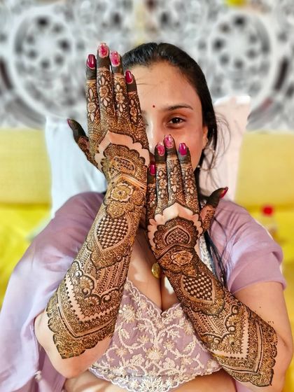 A playful peek from behind her beautifully decorated hands, showcasing the intricate patterns of her engagement mehendi.