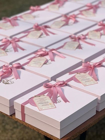 An array of our white gift boxes with pink ribbons and custom tags, prepared for a first birthday party. The uniform look creates a stunning display for large events.