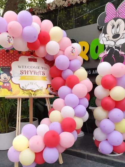 A welcome entrance for a Minnie Mouse party, with a custom sign and a balloon arrangement in classic red, pink, yellow, and purple.