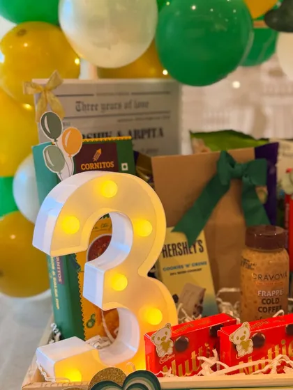 The light-up number '3' is the centerpiece of this anniversary gift, surrounded by treats like Hershey's chocolate and cold coffee. It’s a bright and festive celebration of three years of love.