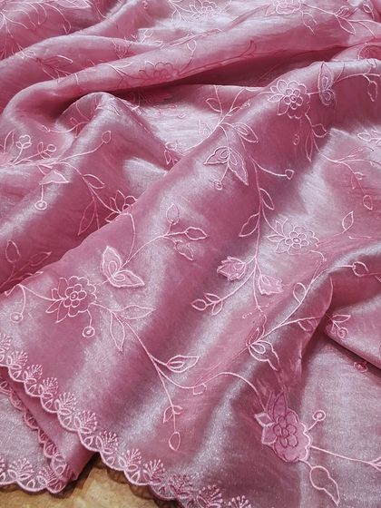A close-up of a pink crush tissue saree with intricate self-colored floral embroidery. The delicate threadwork and scalloped edges highlight the craftsmanship.