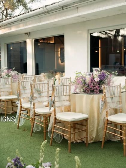 A view of the guest seating arrangement for an outdoor ceremony. The chairs are neatly aligned, and the tables are decorated with floral centerpieces that match the aisle decor, creating a cohesive design.