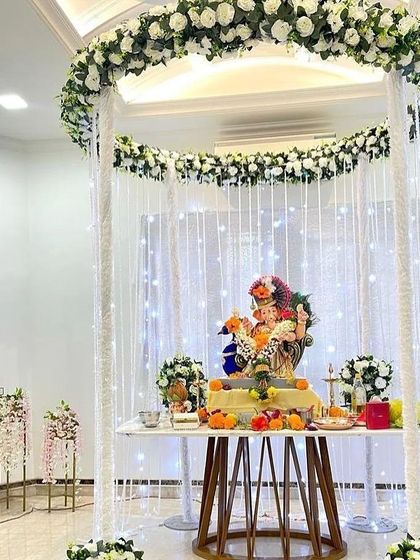 A sophisticated and modern Ganpati mandap with a circular floral halo and hanging strings of crystals and flowers. The all-white theme creates a serene and heavenly atmosphere.