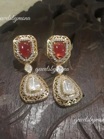 These earrings feature a unique combination of a ruby-colored top and a triangular polki drop, set in a delicate gold frame with jaali work. They are a perfect blend of color and craftsmanship.
