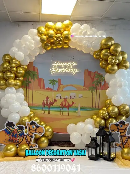 A unique Arabian desert theme. This setup features a custom backdrop of a desert landscape, camel cutouts, and a white and gold balloon arch.