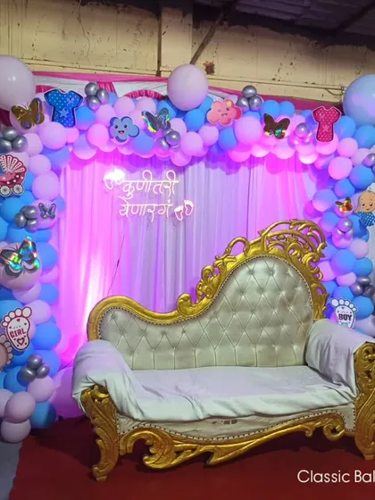 A baby shower stage with a royal golden sofa for the parents-to-be. The backdrop is a pink and blue balloon arch with butterfly and baby-themed foil balloons.