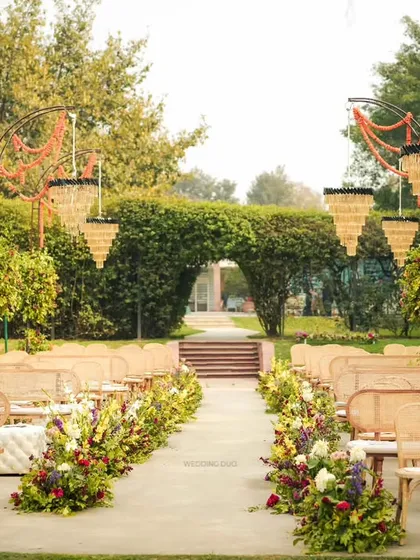 The aisle for this garden wedding was lined with cane benches and flanked by custom arches holding tiered chandeliers and marigold garlands, blending rustic charm with timeless elegance.