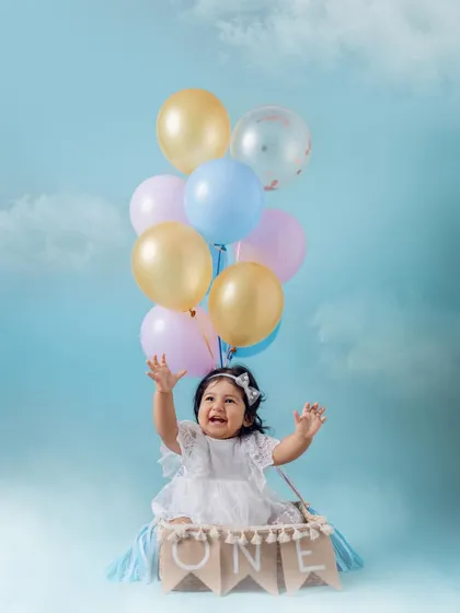 Reaching for the sky. This little girl's excitement is palpable as she enjoys her hot air balloon themed first birthday shoot. The pastel balloons and dreamy backdrop make for a truly magical photo.