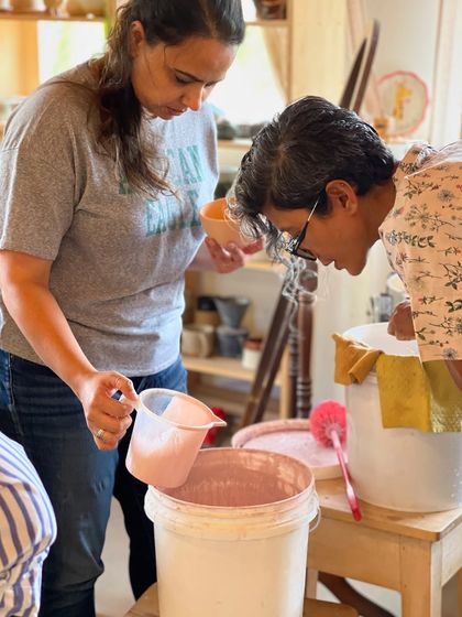 A moment of hands on learning as students gather around to observe the process of mixing glazes.