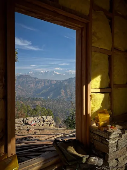 A view from within a guesthouse under construction in Uttarakhand. The wooden door frame and insulation-filled walls frame a stunning vista of the Himalayan range, a constant reminder of the project's incredible setting.