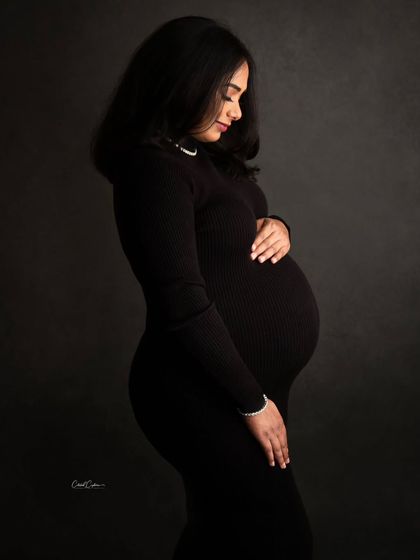 A beautiful side profile that perfectly captures the silhouette of pregnancy. The mom-to-be looks down at her bump with a gentle expression.