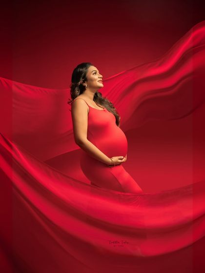 Elegance in motion. This portrait uses a simple red dress and a vast expanse of flowing fabric to create a dreamy, ethereal effect. The upward gaze and soft lighting add to the feeling of serene beauty.