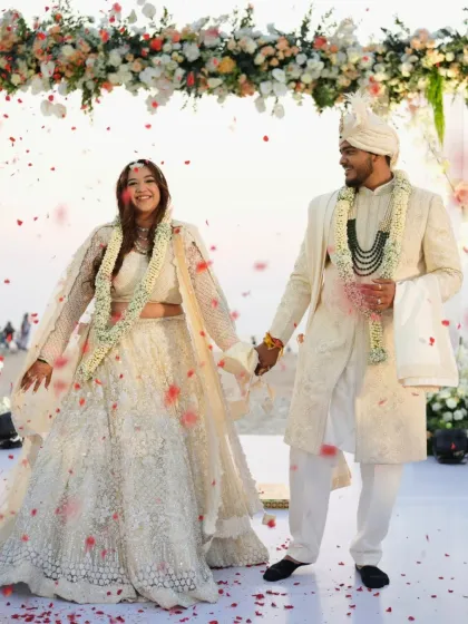 A full-length shot of the couple, hand in hand. The bride's minimal and radiant makeup look is perfect for her elegant ivory lehenga.