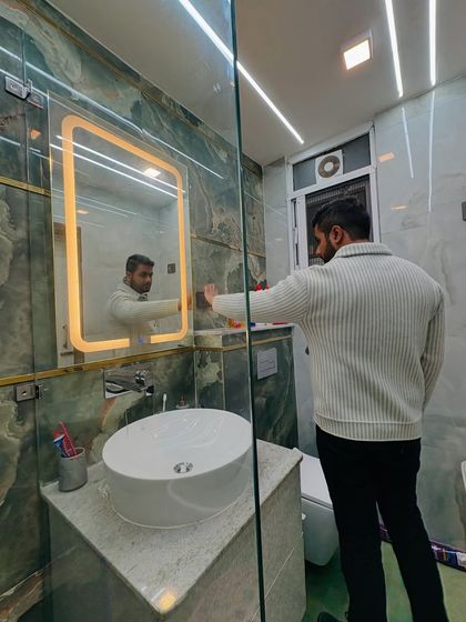 Adjusting the backlit mirror in this newly renovated bathroom. The green tiles with gold inlay add a touch of opulence.