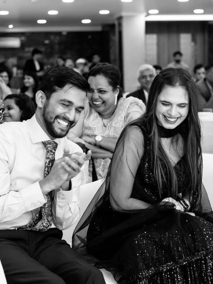 A black and white shot of the couple sharing a heartfelt laugh while watching performances at their cocktail party, a truly genuine moment.