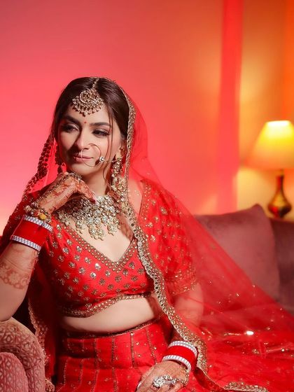 A portrait of a bride in a red lehenga, looking away thoughtfully.