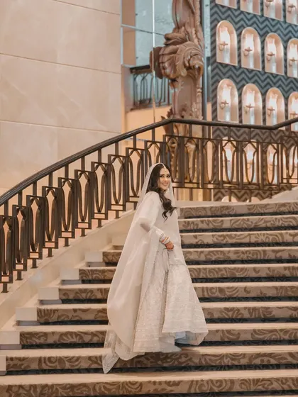 The bride's flowing veil and elegant gown create a beautiful silhouette as she descends the grand staircase.