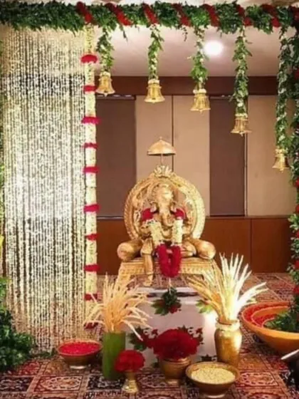 An opulent Ganpati mandap featuring columns wrapped in greenery and red flowers, with curtains of crystal strings and hanging bells. This design blends traditional elements with a touch of glamour.