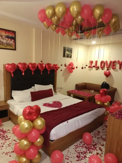 This view highlights the balloon arrangements, including the ceiling balloons, heart-shaped foils on the headboard, and a balloon pillar by the bed.