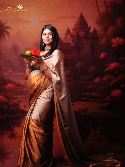 A beautiful portrait of a mom-to-be in a golden saree, holding a plate of fruits. The painterly backdrop and traditional elements create a timeless image.