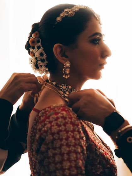 A silhouette of the bride getting her necklace put on. This artistic shot captures the final moments of preparation in a cinematic way.