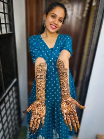 A happy bride showing off her full narrative henna, complete with bride and groom figures.