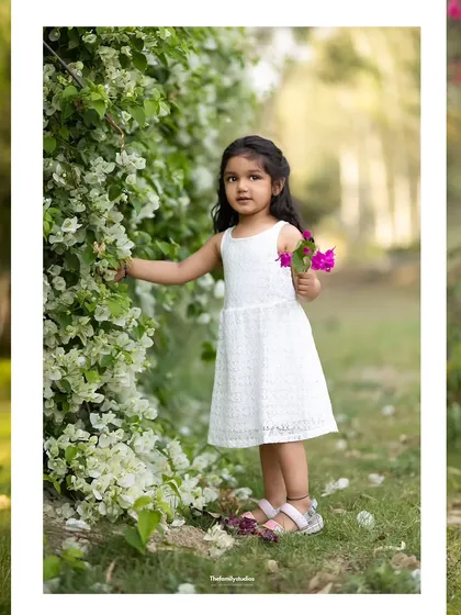 This portrait captures a young girl interacting with a wall of white flowers. Our outdoor kids' photoshoots focus on letting children explore their surroundings naturally.