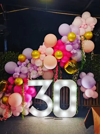 An outdoor 30th birthday decoration with large marquee numbers. The numbers are framed by a beautiful organic balloon garland in shades of pink and gold.