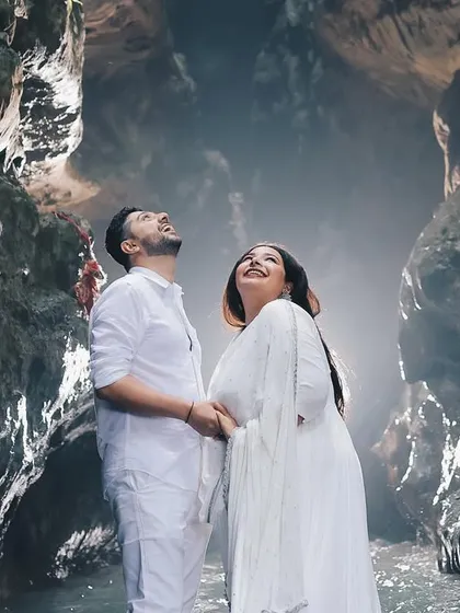 The couple looks up in awe inside a stunning natural cave, with light filtering in from above. This is an example of a truly unique pre-wedding location shoot.