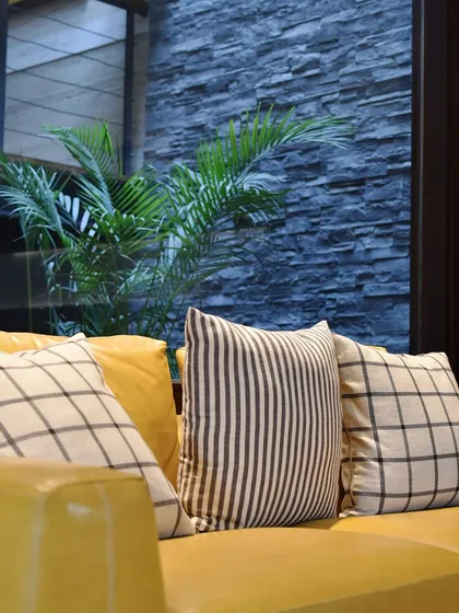 A vibrant yellow leather sofa brings a bold pop of color, set against the serene backdrop of an indoor court with a natural stone wall. This is a perfect blend of nature and modern design.