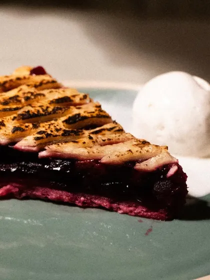 A slice of warm cherry pie with melting ice cream. The moody lighting creates a cozy, comforting feel, perfect for a diner menu.